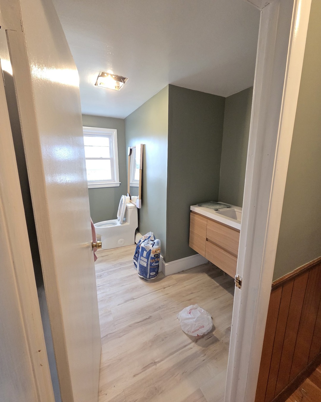 Finished bathroom remodel with a floating wood vanity, sage green walls and light wood plank flooring