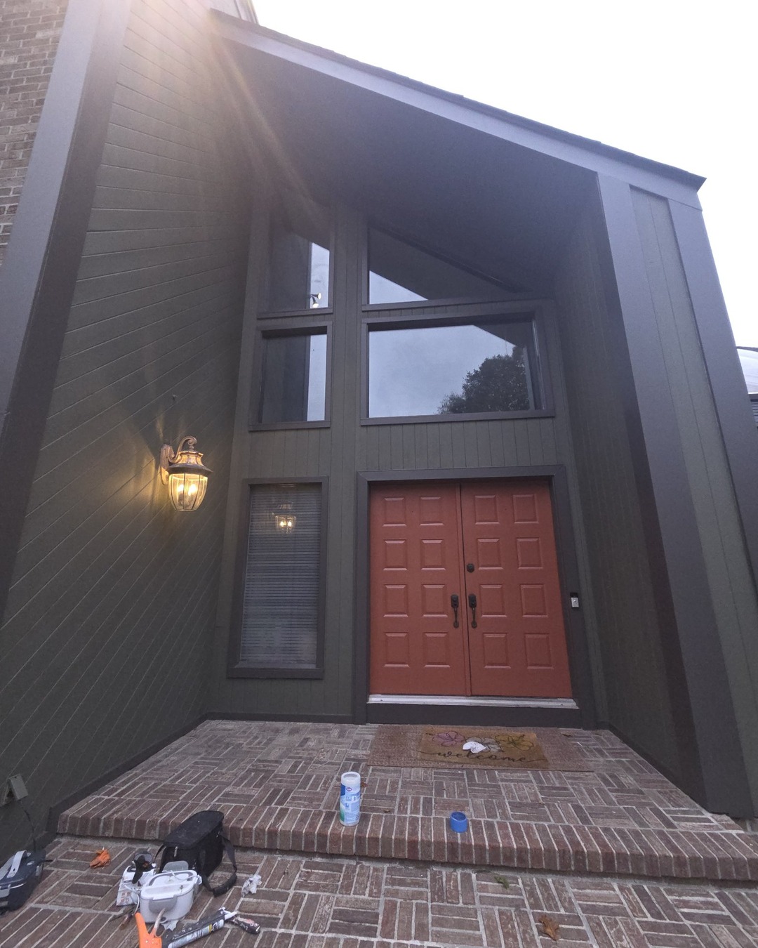 Front entryway in fresh dark olive green with rust-red doors and caulking supplies on the brick steps