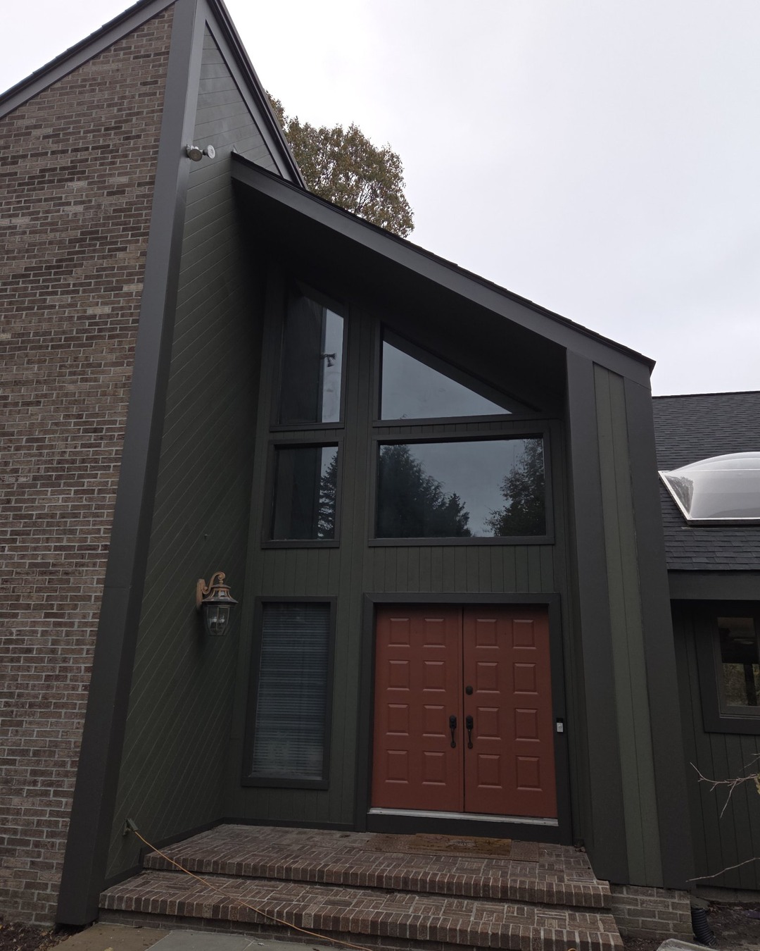 Finished front entryway with dark olive green siding, rust-red double doors and brick porch steps