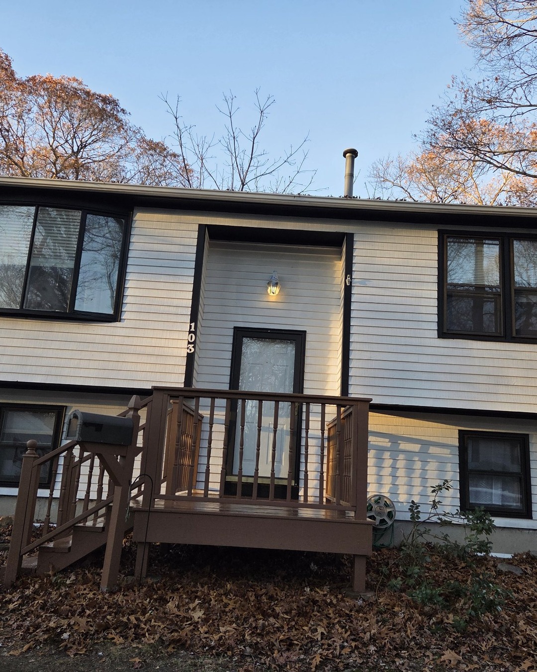 Front entryway of the shingle home after painting, with white siding, dark brown trim and window frames and a wooden entry porch and stairs